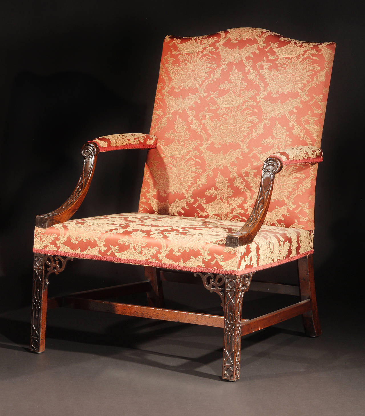The padded serpentine back issuing downswept arm supports; raised on square chamfered legs finely carved with blind fretwork with pierced brackets and joined by a conforming H-form stretcher.