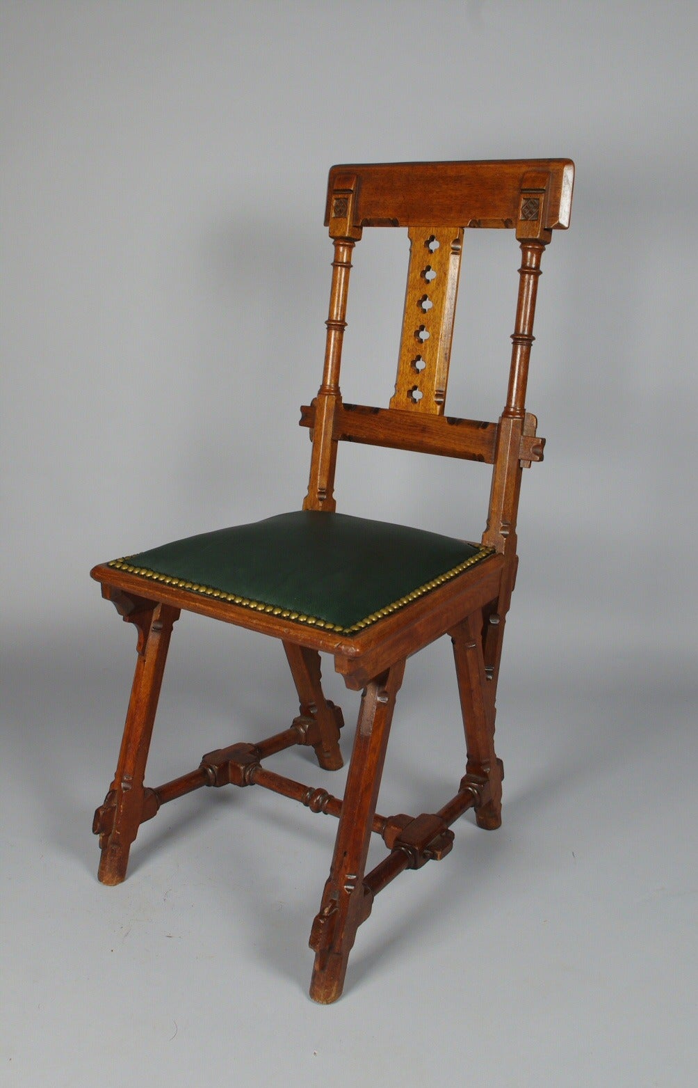 Kimbel and Cabus walnut modern Gothic side chair, the tablet crest rail let into the stiles over the splat with pierced quatrefoils; the seat, newly upholstered in green leather with brass tacks, on canted legs joined by an H-stretcher, with overall