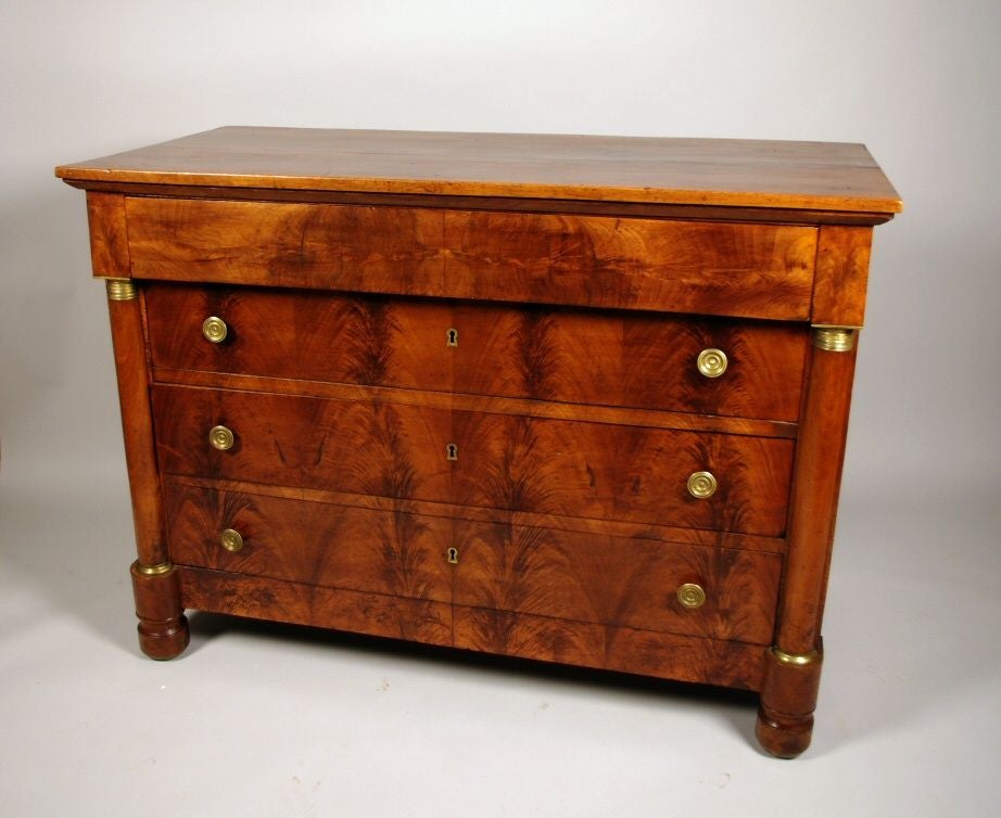 Empire walnut chest of drawers, the solid rectangular top over a single long drawer with concealed handles, over three long drawers, each with well chosen bookmatched veneers and later brass hardware, flanked by a pair of applied half columns with