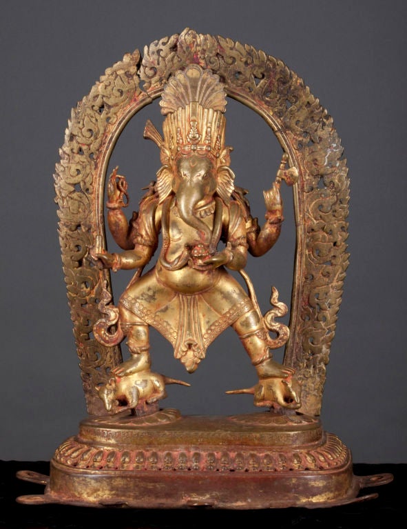 A fantastic Nepalese Ganapati who in this example is crowned, four-armed, has a serpent around his neck (as in Purana texts), stands astride his two rat totems, and is surrounded by a flaming mandorla. His hands hold a mala, his broken tusk, an ax,