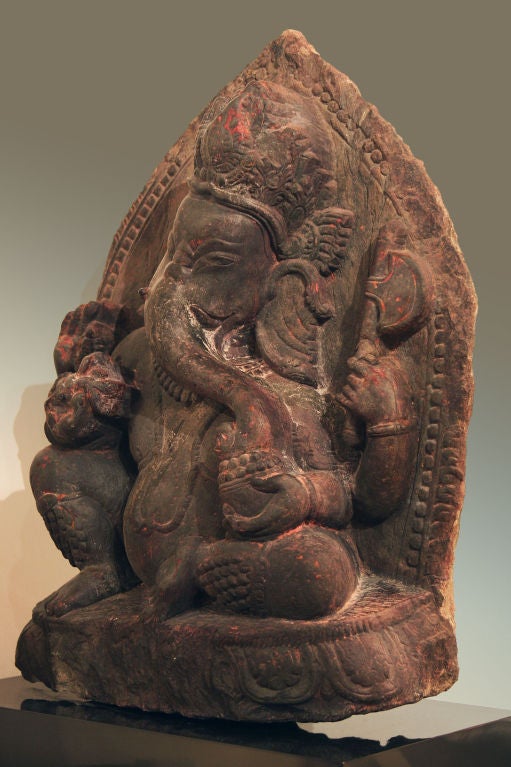 Obviously revered, this Nepalese seated Ganesha still bears the traces of red sindura, the devotional powder sprinkled on such images as a sign of respect. With his four arms and hands holding traditional implements such as prayer beads and an axe,