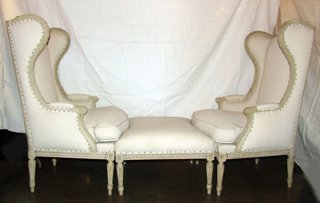 Beautifully Handcarved! Duchesse Brisee comprising two His/Hers Wing Chairs and Ottoman in Louis XVI Style.  Each chair with arched upholstered back centered by pair carved flowers on twisted acanthus ribbon crestrail flanked by scrolled wings over