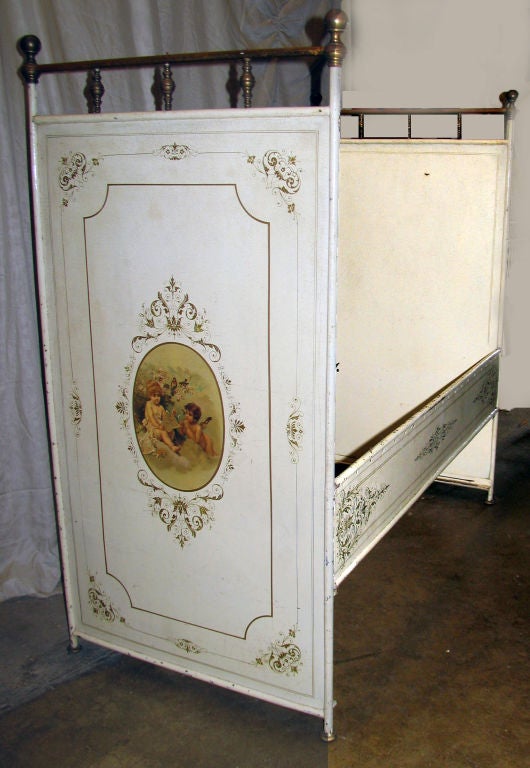 Delightful French white painted tole childs bed with brass rail and charming handpainted panels depicting a pair of kissing cherubs and a pair of cherubs reading with gilded scrolled borders and decoration.