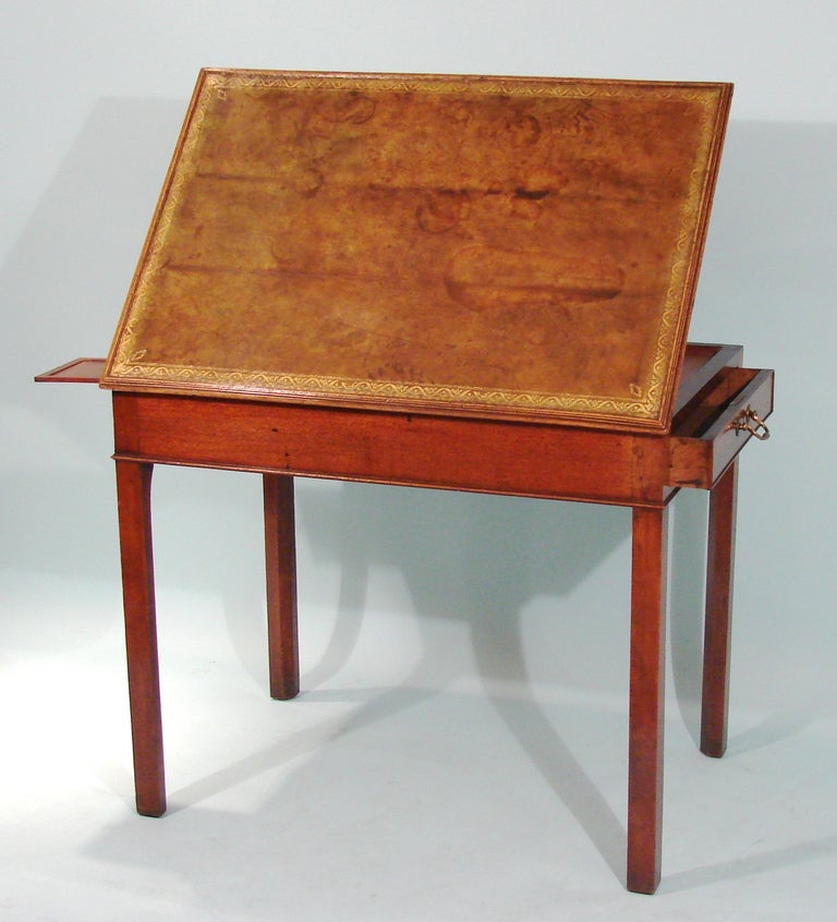 George III mahogany artist's or drafting table, the gilt tooled leather lined top with ratchet mechanism adjustable to varying angles over 2 side drawers and a later concealed candle slide all on square legs.