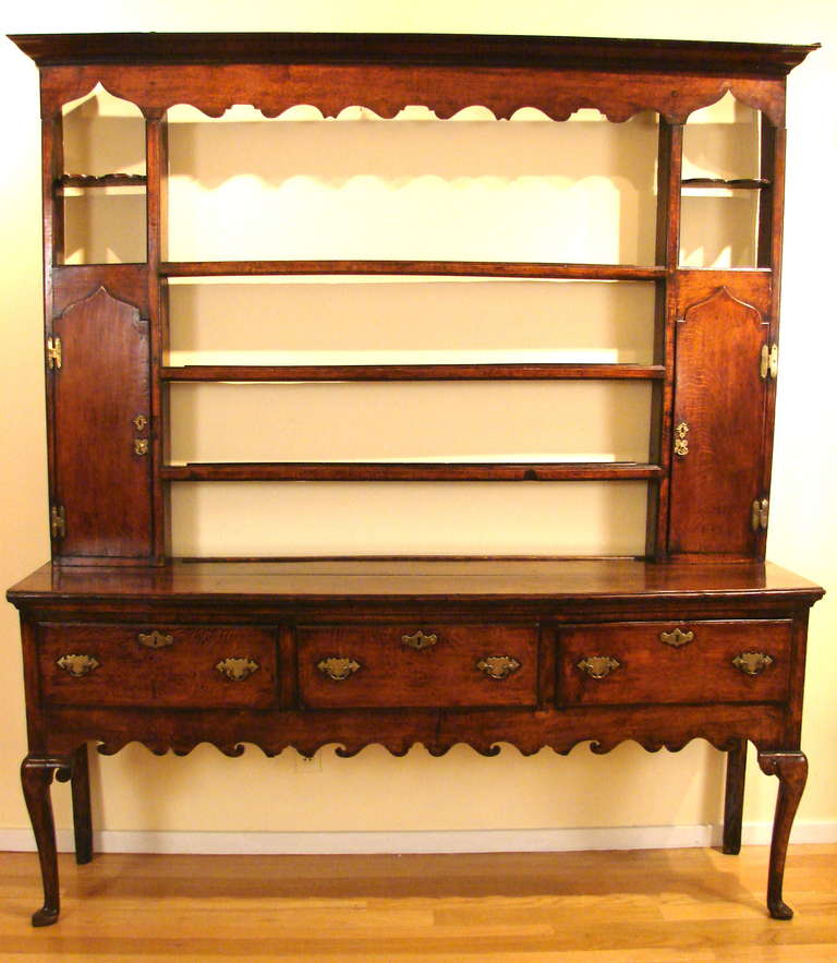 A good quality oak high dresser in 2 parts, the upper stage with 2 short and 3 shelves, flanked by cupboard doors, the lower with 3 drawers supported by front cabriole legs centered by a scalloped apron. Hardware appears to be original. Wonderful