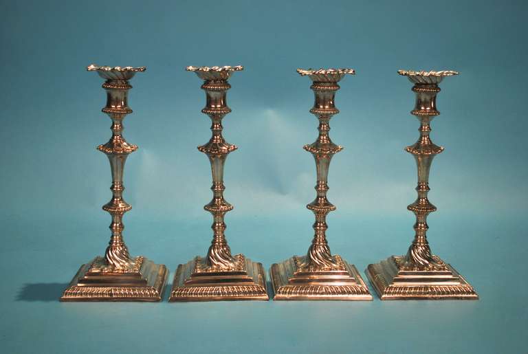 A rare and attractive set of 4 Georgian sterling silver cast candlesticks each on a square base with knopped stem and spool-form socket, with removable nozzle, gadrooned borders throughout, fully marked on bases and sockets. Made by the well-known