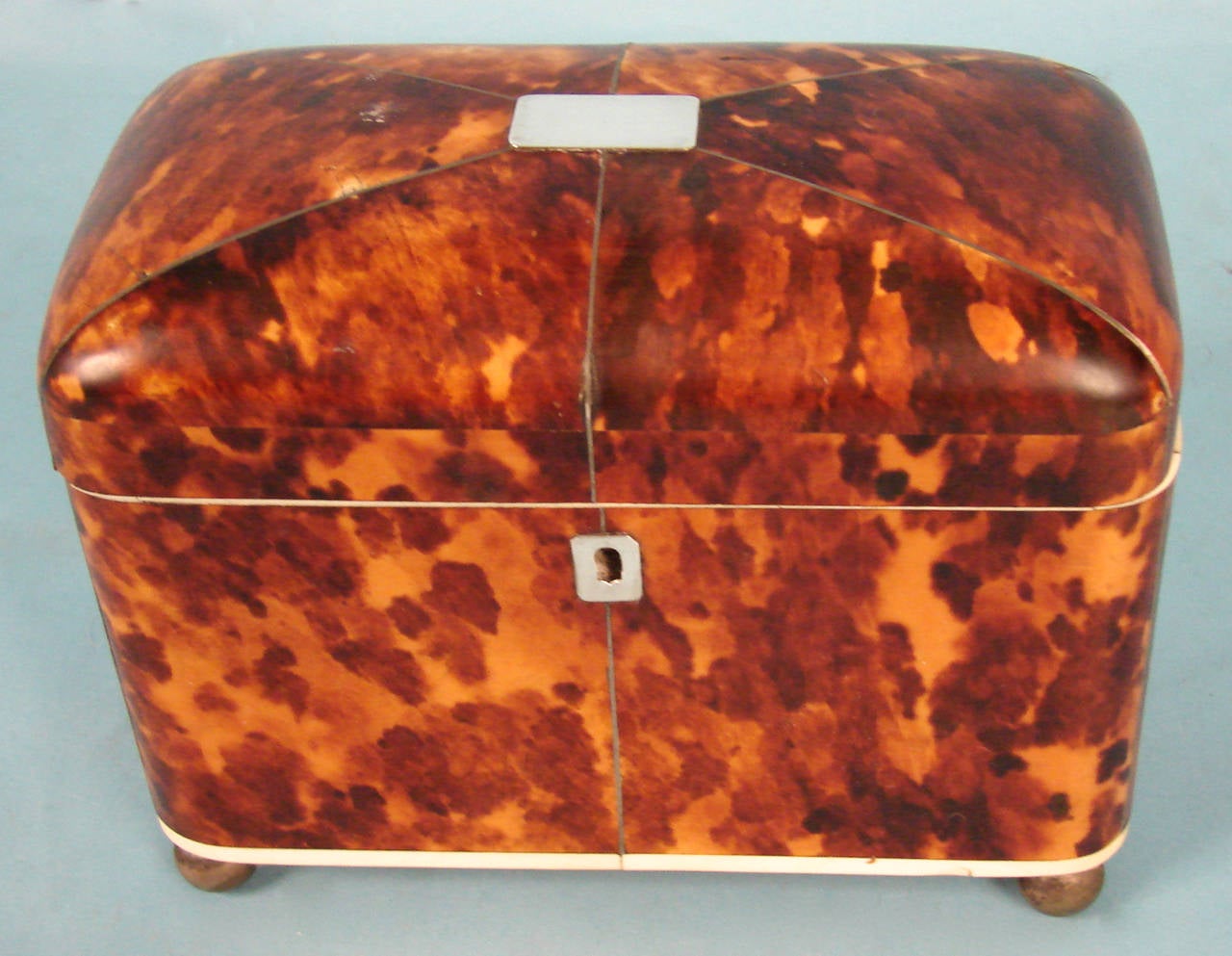 An attractive Regency period tortoise shell tea caddy the top inlaid with a silver central piece and with pewter stringing, the divided interior now with a marbleized paper lining and two lids, all resting on silvered ball feet.