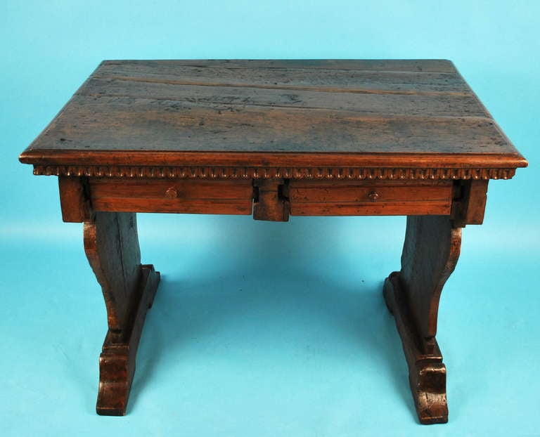 An  Italian late Renaissance period writing table, the plank top with a molded edge over a further thumbnail edge above 2 drawers, supported by shaped sides ending on plinth supports.