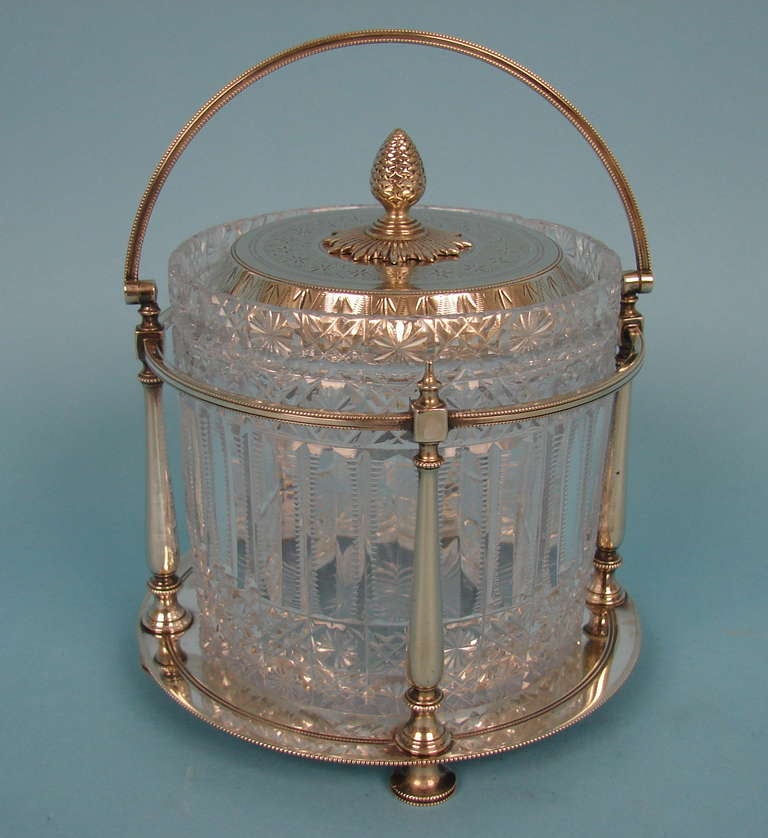 An English silverplate and cut crystal lidded jar, the engine turned top with a  pineapple finial, the handled frame with columnar supports terminating in bun feet. Made and hallmarked by James Dixon & Sons.