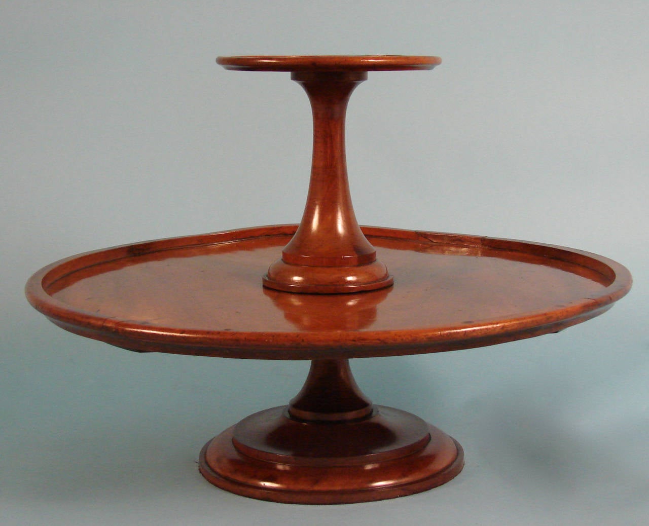 An English mahogany two-tier revolving server, each section with an applied edge, supported on a conforming base, circa 1880.