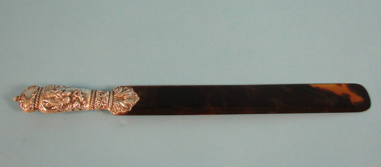 A pretty English tortoiseshell paper knife or page turner, the sterling chased handle hallmarked for London, 1902 maker WC, depicting a loving couple in traditional dress with cupid overhead, the blade made of red tortoiseshell.