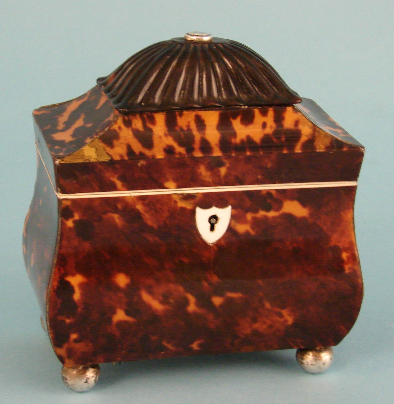 A good English pagoda form tortoiseshell tea caddy, the pressed shell dome centered with a silver boss over a shaped lid, resting on a bombe form base with an ivory keyhole escutcheon, on silvered ball feet.