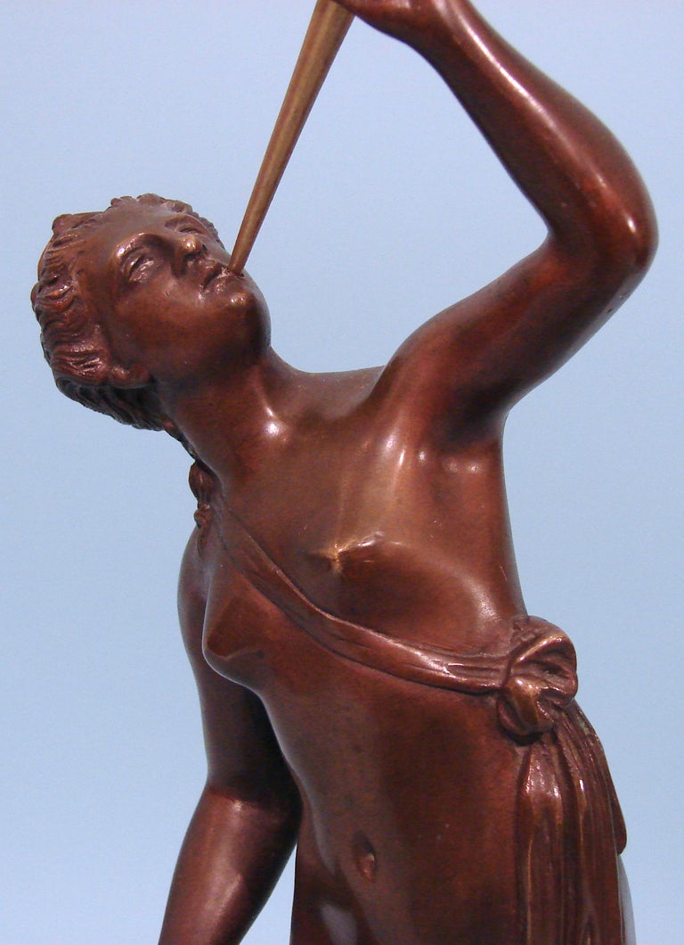 A 19th century Continental bronze figure of a nude holding a brass horn all emanating from a face mounted on a turned slate socle decorated with  gilt bronze relief.