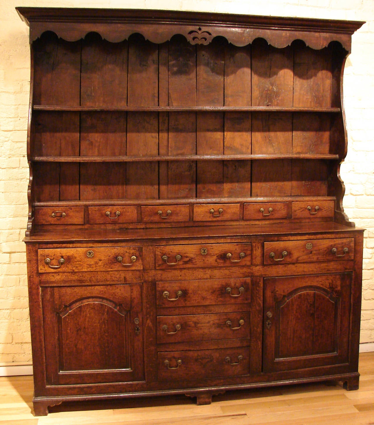 A fine and large English or Welsh oak high dresser, the upper stage with three shelves and six small drawers under a scalloped hood with central decoration, resting on a base with six drawers and two cupboards with fielded panel doors all on bracket