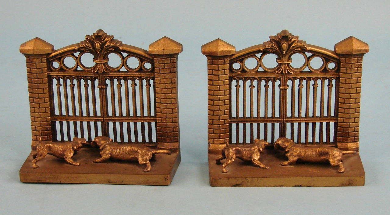 An amusing pair of Bradley and Hubbard gilt bronze figural bookends depicting anxious hounds poised at a large gate, circa 1900-1915.