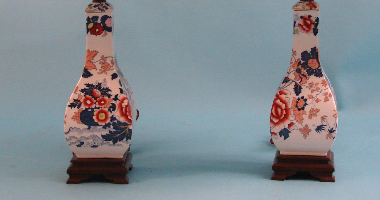 A pretty pair of English ironstone bottle form vases decorated overall in a floral motif of blues, red and pink, now electrified and resting on wooden bases, circa 1850.