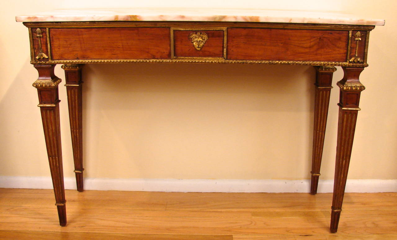 An Italian neoclassical parcel-gilt walnut console table, the Sienna marble top above an apron with beaded edge centered by a classical face with stylized floral corners, supported on fluted square tapered legs, circa 1790.