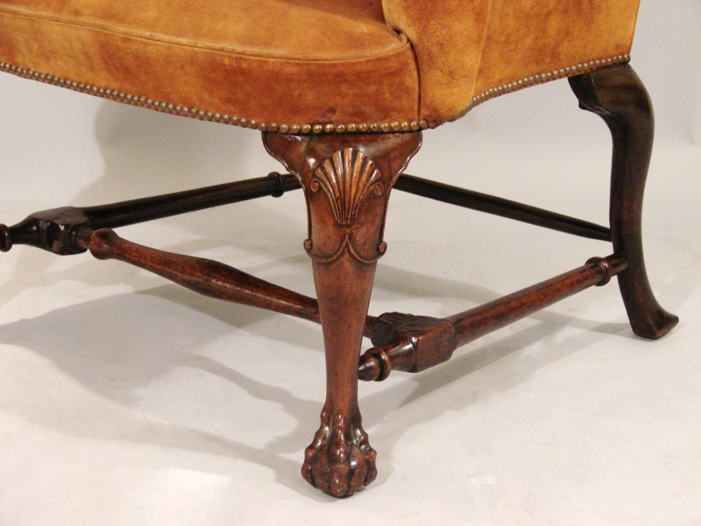 A pretty George II period walnut wing armchair, the shaped back over cabriole legs with shell carved knees ending in ball and claw feet joined by a turned stretcher. Rear legs spliced, repairs. Circa 1730. Now upholstered in brown suede.