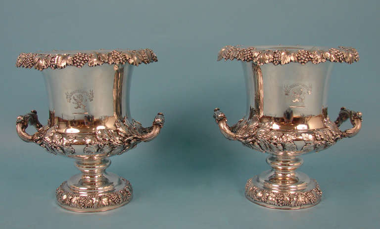 A pair of Sheffield silver plate wine coolers, each having a repousse decorated grape vine rim continuing to the body having naturalistic handles accented with an oak leaf motif flanking a central inscribed motto above a rampant lion, rising on a