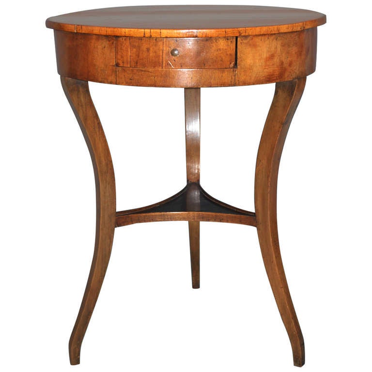 A Northern European walnut veneer round occasional table with centered by a shelf, the apron containing a single  drawer supported on downswept legs.