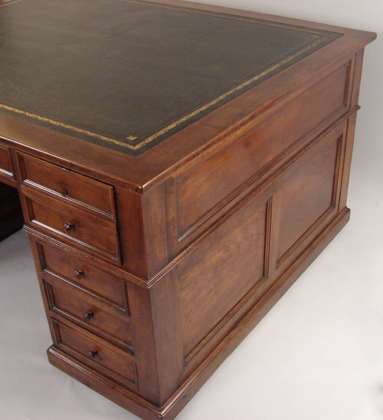 A French walnut partners desk with paneled sides, the green gilt-tooled leather top above three frieze drawers, one long and two short, above six additional short drawers on the front and cabinets on the back, resting on a plinth base with later