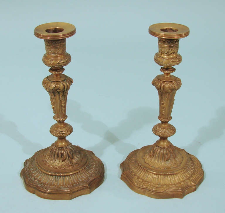 A pair of Louis XVI gilt bronze candlesticks with inverted baluster standard supporting cylindrical nozzles on domed feet, cast all-over with flutes, acanthus and ribbon bound reeds, circa 1800-1820.