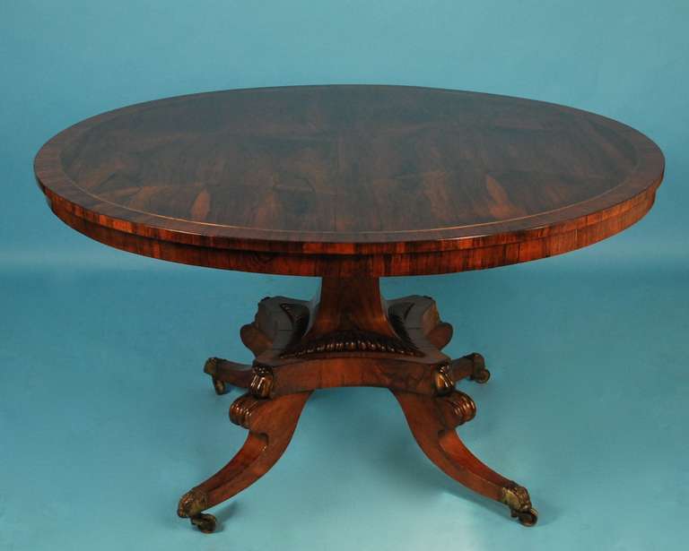 A pretty rosewood tilt-top center table, the crossbanded figured top inlaid with brass stringing, the sculpted quadripartite base with parcel gilt scrolled knees and down swept legs ending in brass caps with casters.