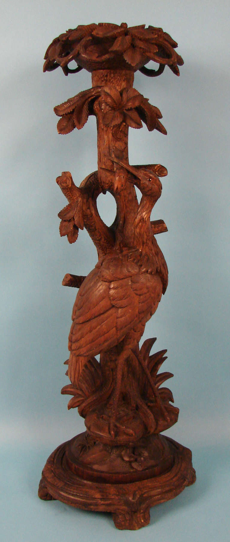 A fine and rare Black Forest carved torchere or plant stand in the form of an Ibis with a fish in its mouth all in a naturalistic setting.