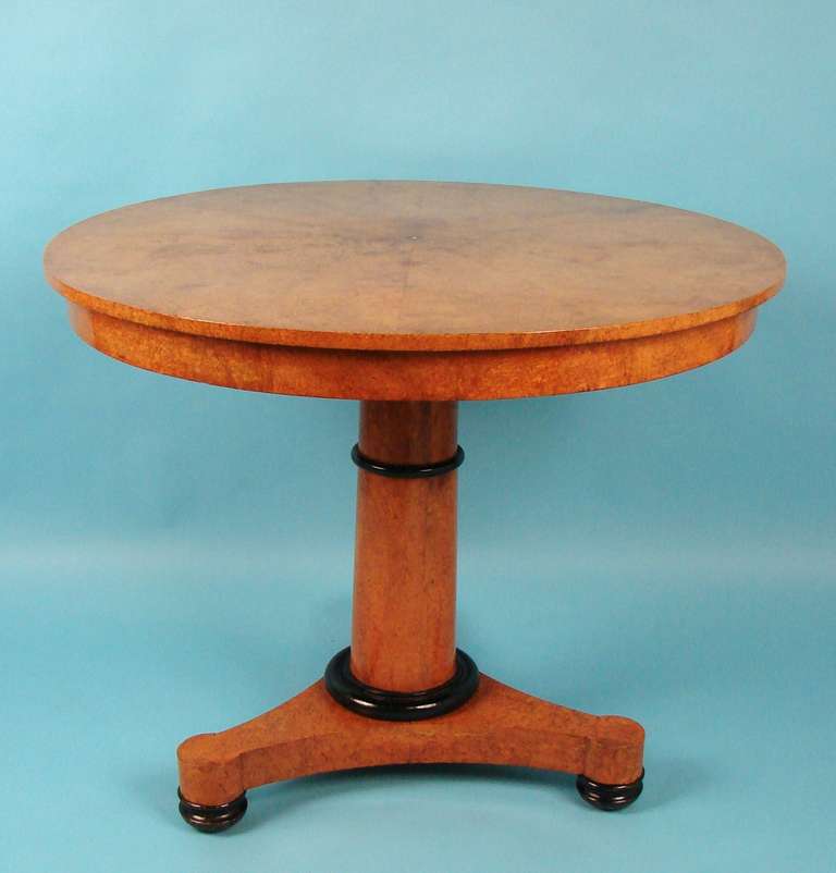 A pretty burr ash or elm Northern European round occasional table, the pie sectioned venered top above a partial ebonized columnar standard ending in a tripod base with bun feet and concealed casters.
