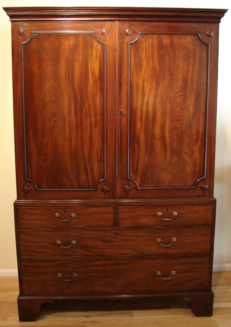 A Georgian III mahogany linen press the paneled cupboard doors opening to reveal 3 of 4 original interior slides, the upper section over 2 long and 2 short drawers on later bracket feet.