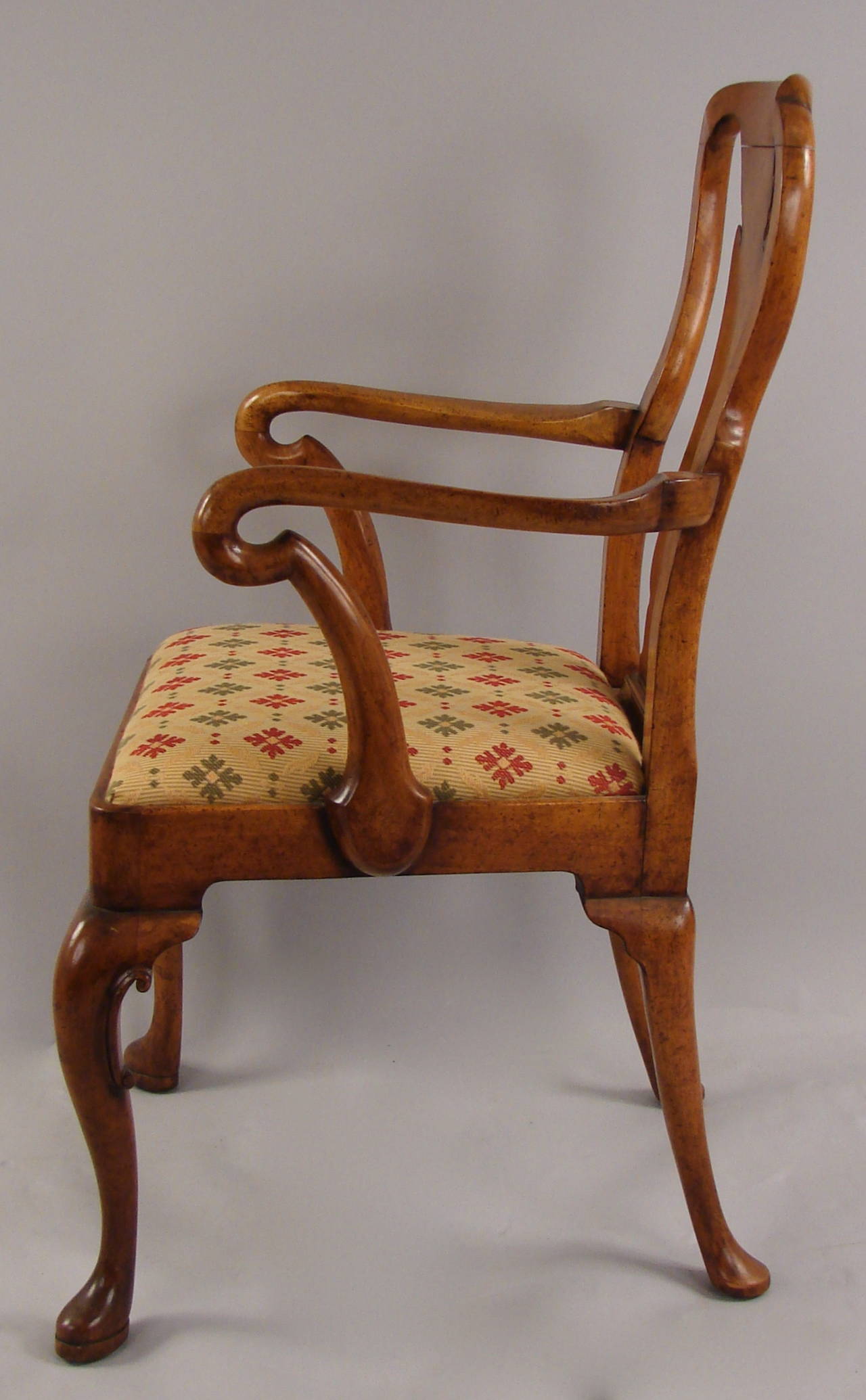 A pair of Queen Anne style walnut arm chairs each with a curved crest rail surmounting the vasiform splat above drop in seats on a shaped apron raised on cabriole legs, circa 1890-1900.