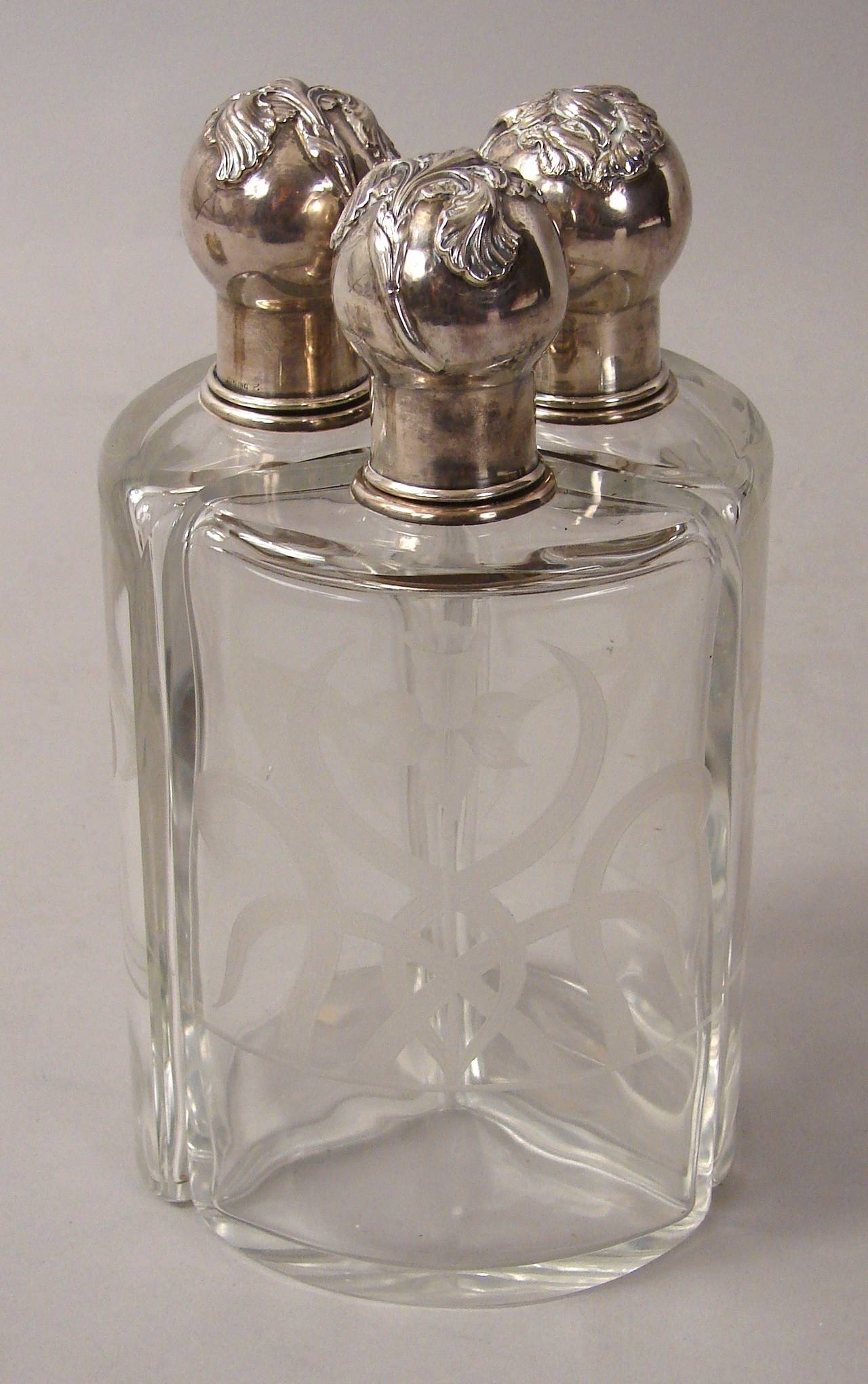 A rare and unusual set of three Shreve Art Nouveau etched glass decanters with sterling silver iris motif lids, fitted in a sterling silver floral decorated base. Collars and base signed 