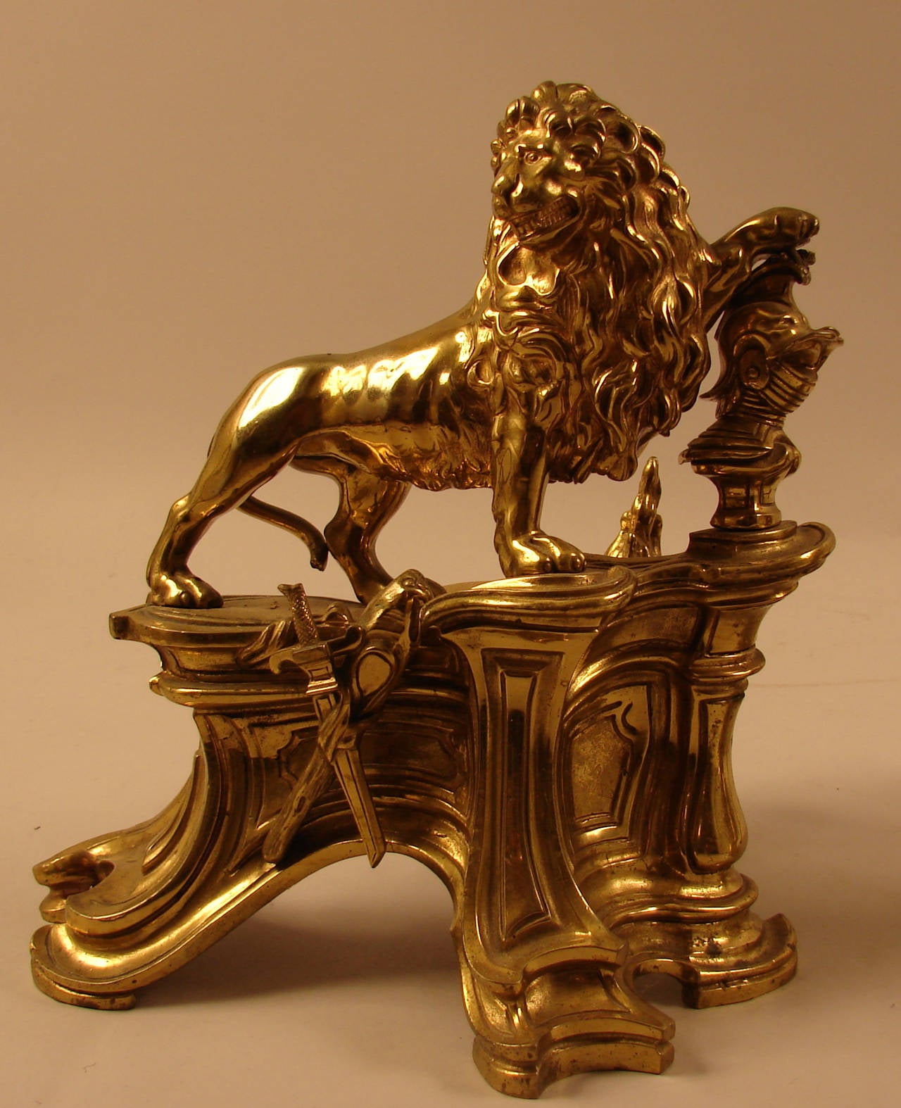 A fine pair of beautifully made bronze or brass chenets, the naturalistically modeled lions in a lively posture with expressive faces, one holding a shield, the other a knight's helmet resting on stylized plinths, 19th century.