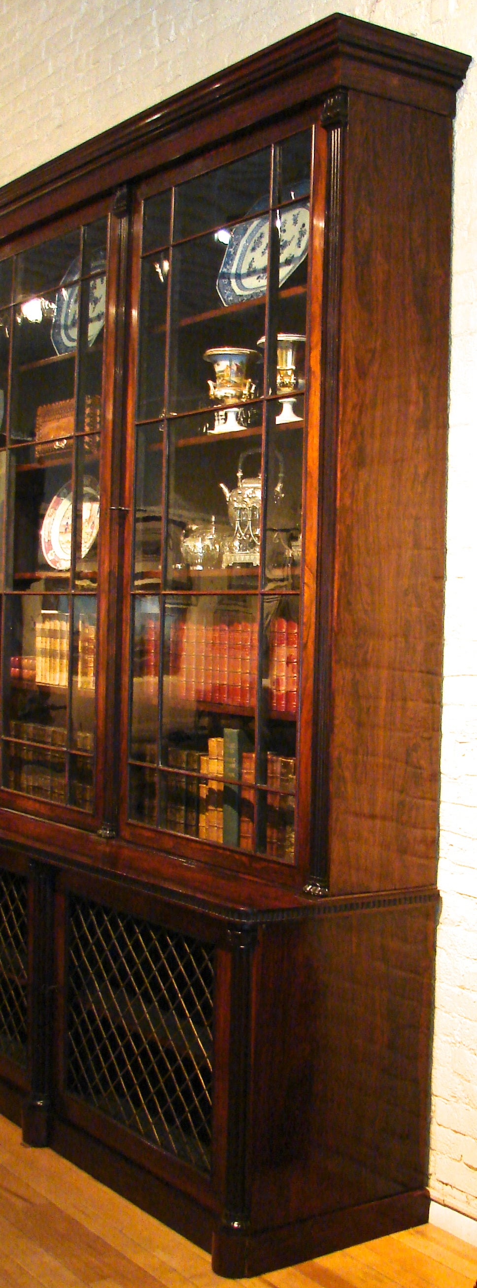 A magnificent and substantial Regency period rosewood brass-mounted bookcase, the overhanging molded cornice above a pair of astragal glazed doors flanked by fluted columnar supports, the lower section with a pair of brass grill cupboard doors and