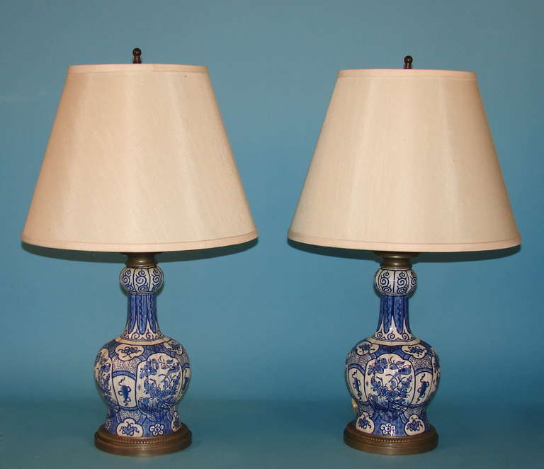 An attractive pair of blue and white bottle neck Delft vases with white metal fittings, typically decorated, now electrified as lamps.