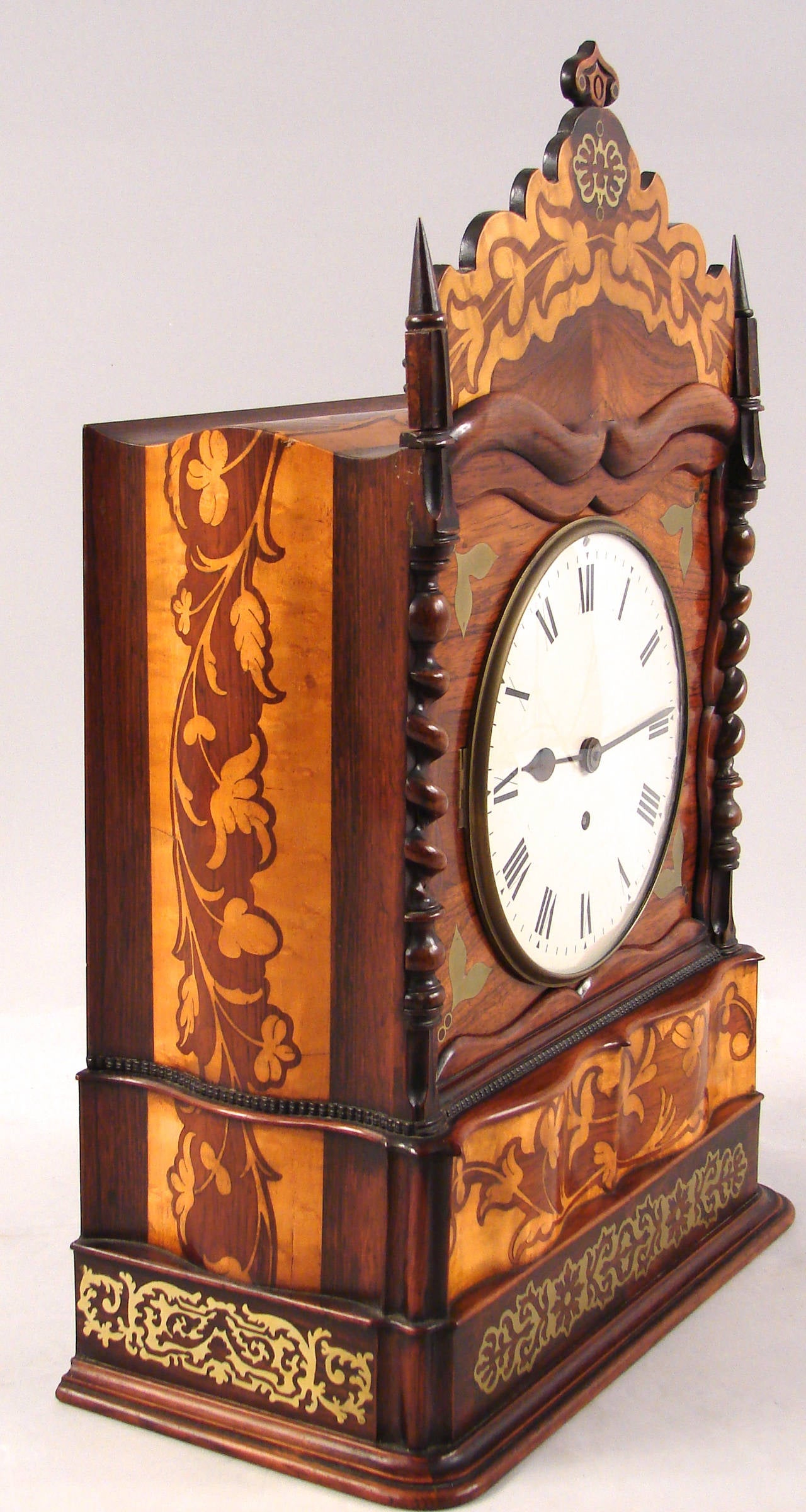 An unusual and rare Irish (Killarney) arbitus, yew wood, satinwood inlaid 8 day movement clock of architectural form, the removable cresting above a simple dial with Roman numerals flanked by twisted columns on a foliate inlaid plinth. Recently