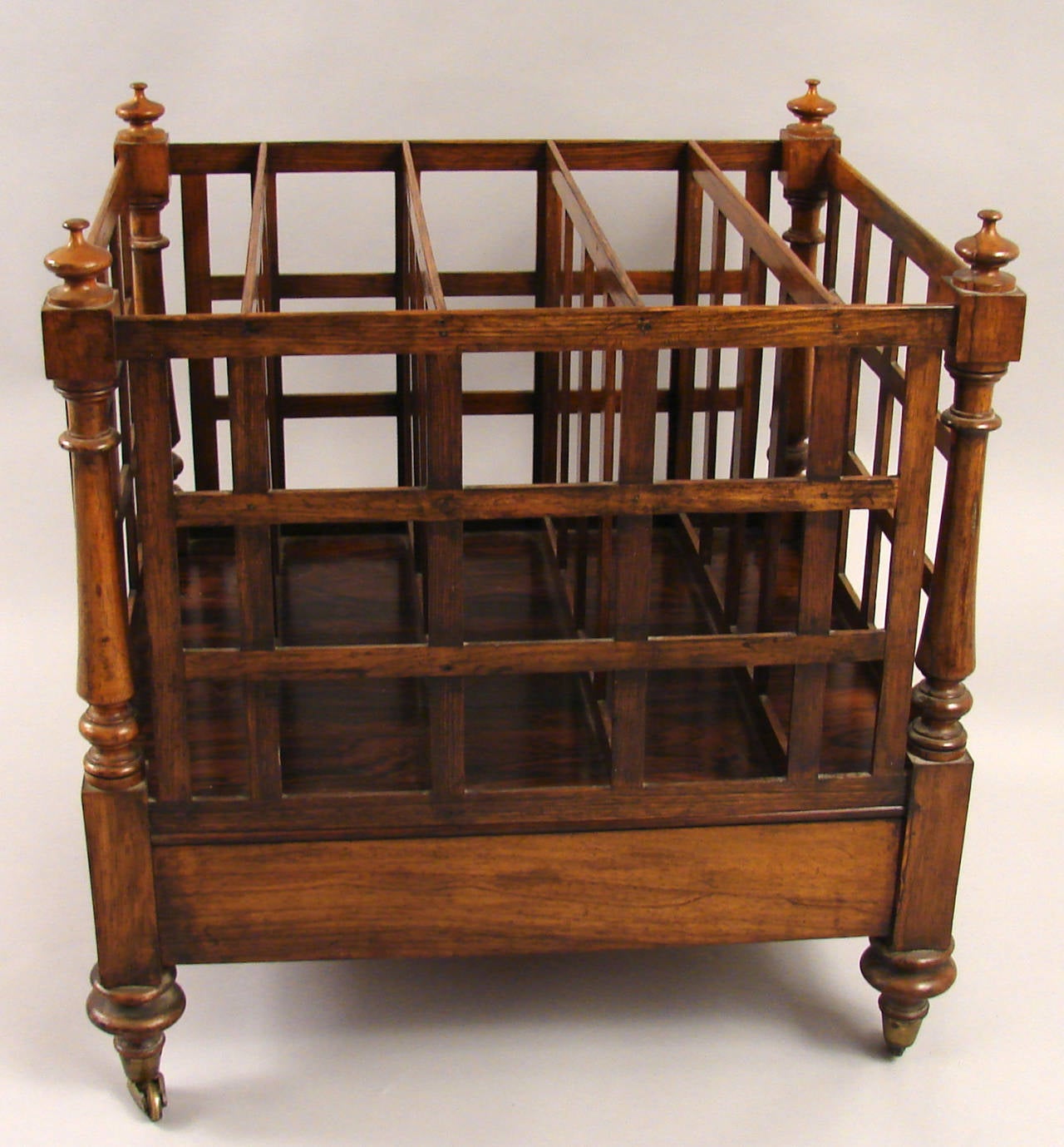 A large-scale Regency rosewood Canterbury having five flat-topped partitioned compartments with finial top corners rising on turned legs terminating on casters. One functional side drawer, circa 1820.