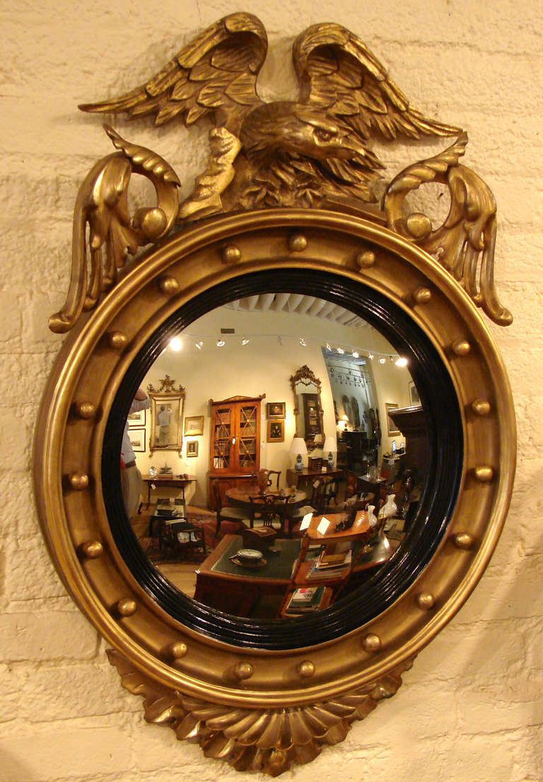 An English Regency period  bull's eye mirror of typical form, with eagle cresting, the convex plate with ebonized banding surrounded by 19 balls with acanthus leaf decoration at the bottom.