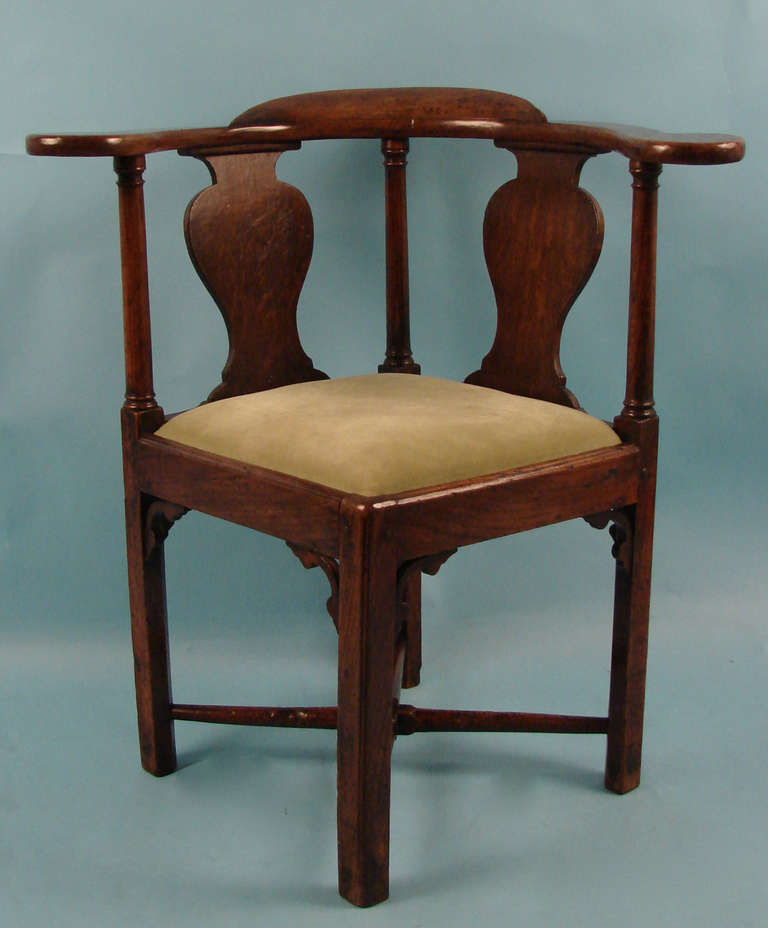 An English provincial oak corner chair of typical form, the vasiform splats above a straight seat with delicate corner brackets resting on square legs joined by a turned stretcher. Circa 1770.