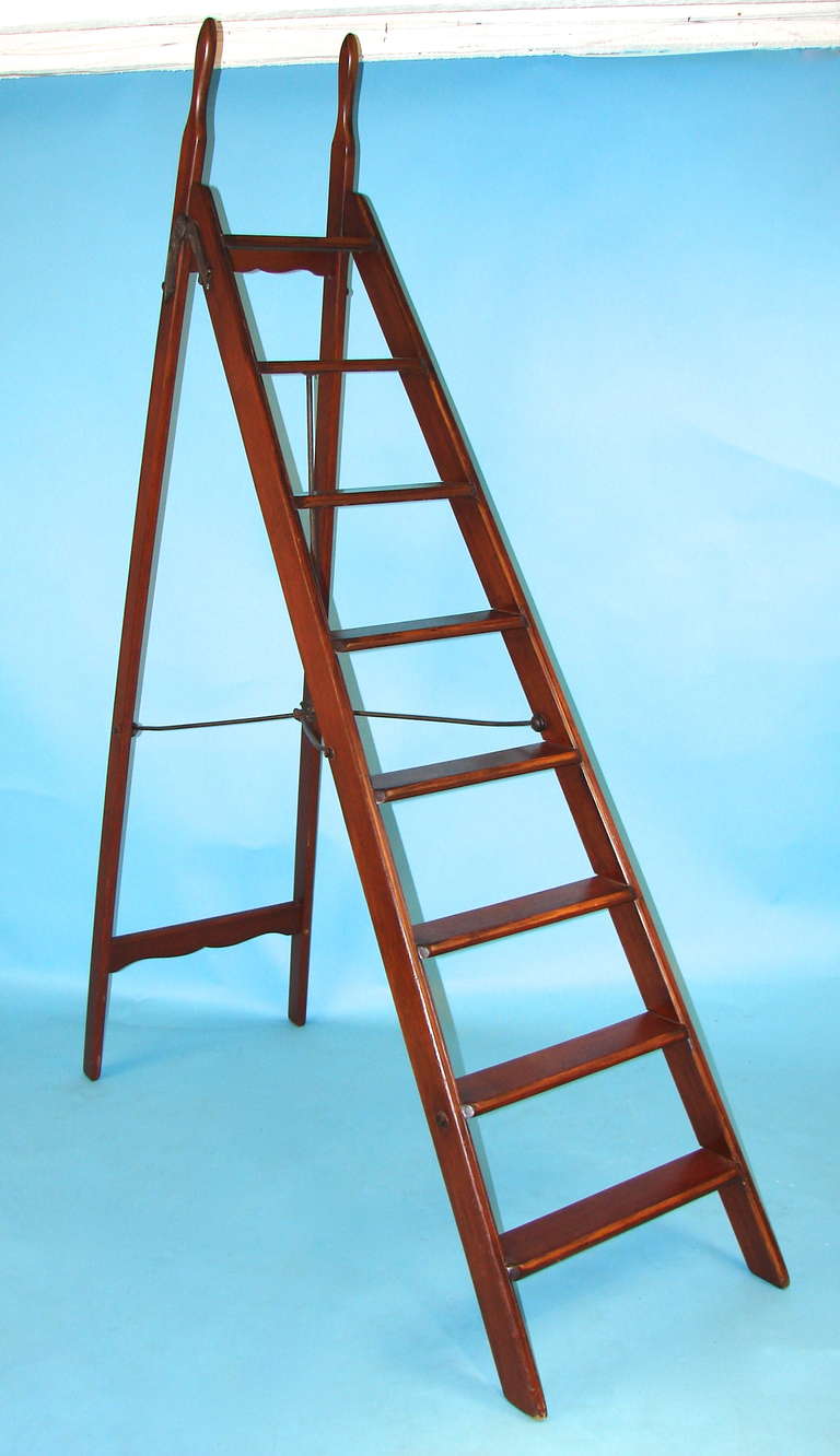An English mahogany collapsible library ladder with cast iron braces and mounts and carrying handles at the top.
