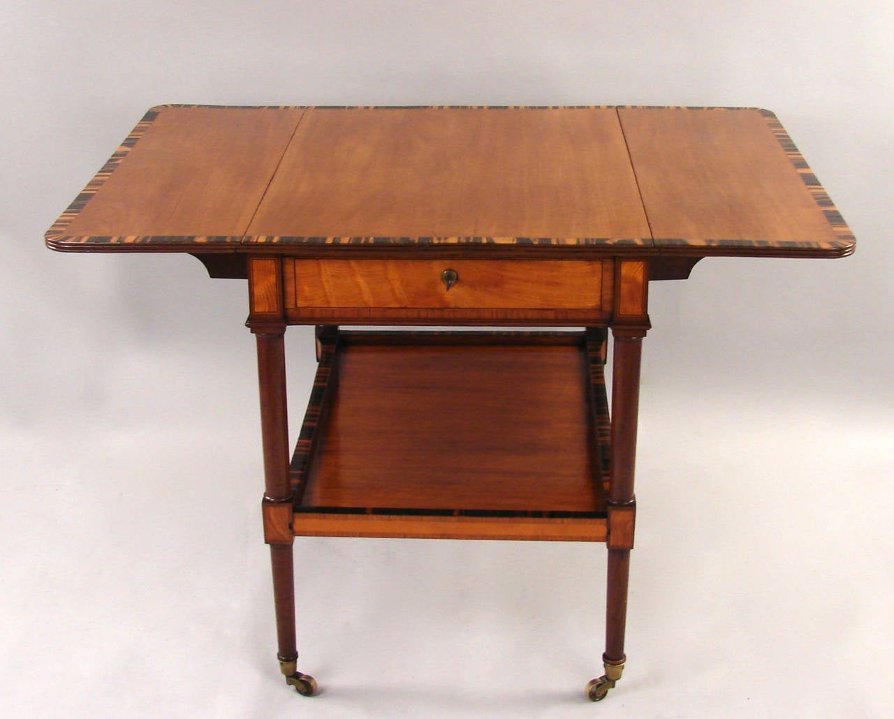 A fine quality George III inlaid satinwood pembroke table, the calamander or zebra wood crossbanded top above a single drawer, with a similarly inlaid moveable shelf below, supported on turned tapered legs terminating on casters, circa 1800.