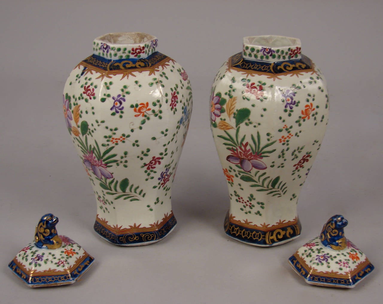 A pretty pair of French porcelain hexagonal form lidded vases decorated with lavender and rose peonies and floral sprigs, the blue and gold trimmed lids surmounted with a blue fu lion finial, circa 1900.