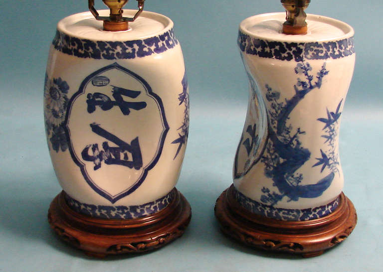 A pair of Chinese porcelain blue and white pillows with overall calligraphy and foliate decoration resting on carved wooden bases, now electrified. Circa 1900.
