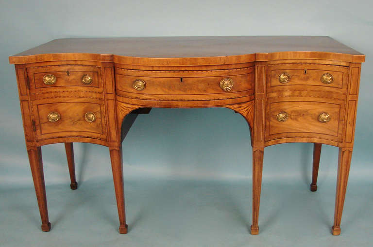 An extremely fine George III period inlaid mahogany sideboard, the figured mahogany serpentine top above a conforming case with a central drawer flanked by a satinwood inlaid apron, the left side a cupboard door, the right a deep drawer, all