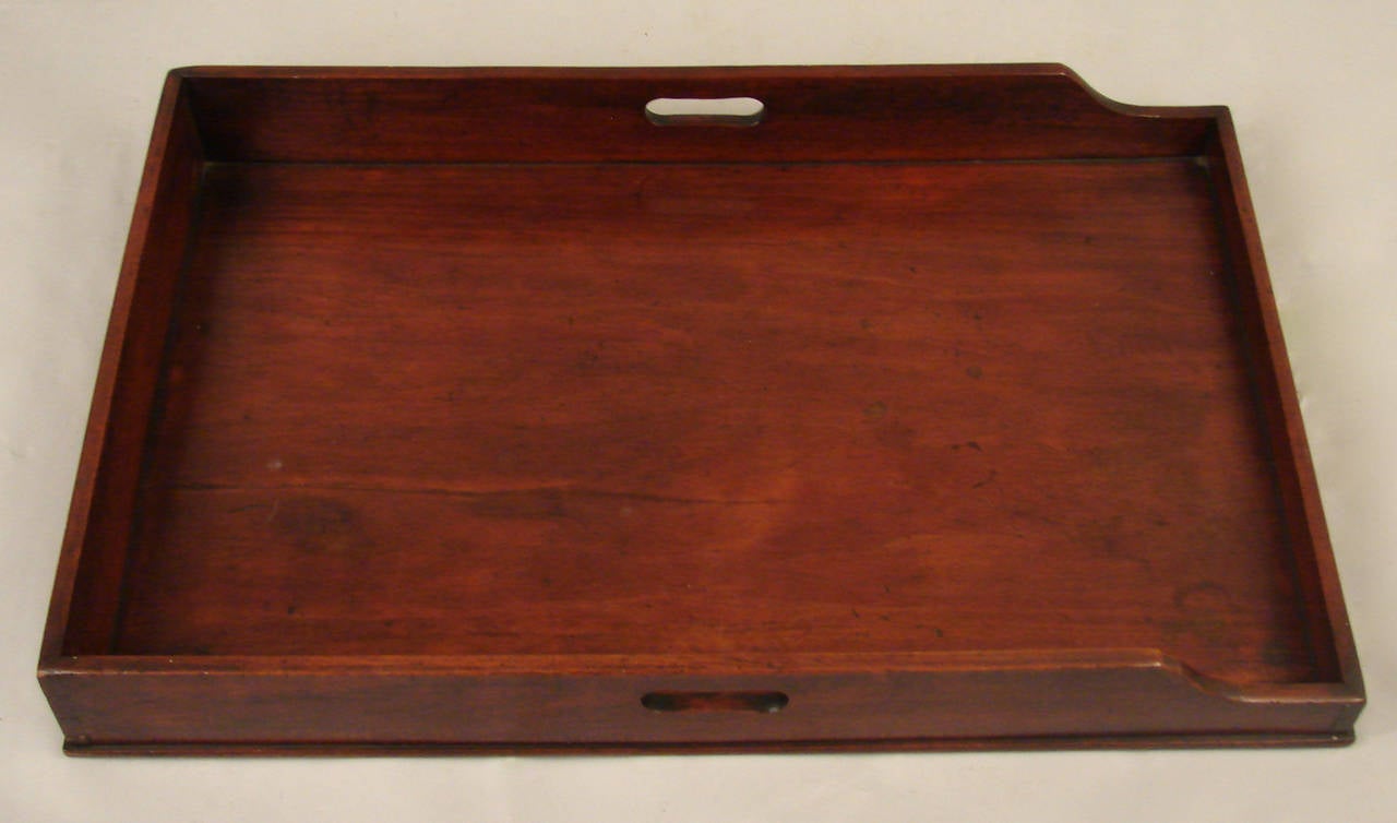 An English mahogany butler's tray with shaped sides and cut out handles now on an associated folding mahogany stand of a later date. Tray dates from the first half of the 19th century.