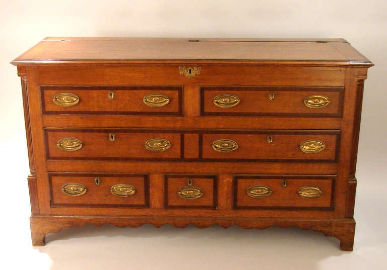 An English oak mule chest with reeded quarter columns, the lift top over one long and three short mahogany cross-banded functional drawers above a shaped apron on bracket feet.