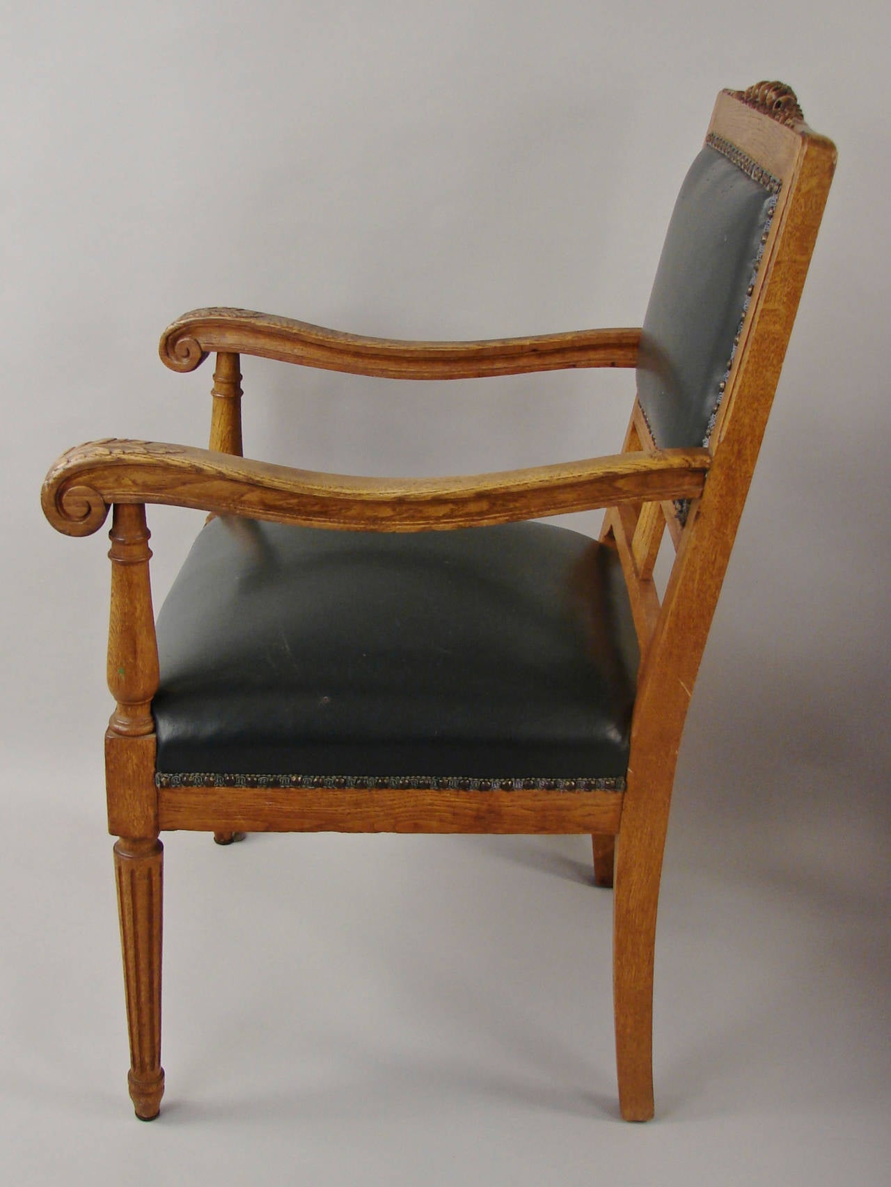 A pair of late 19th century German oak dark green leather-upholstered armchairs, the crest rails with carved floral motifs, the arms with carving at the knuckles, supported on fluted front legs, circa 1880.