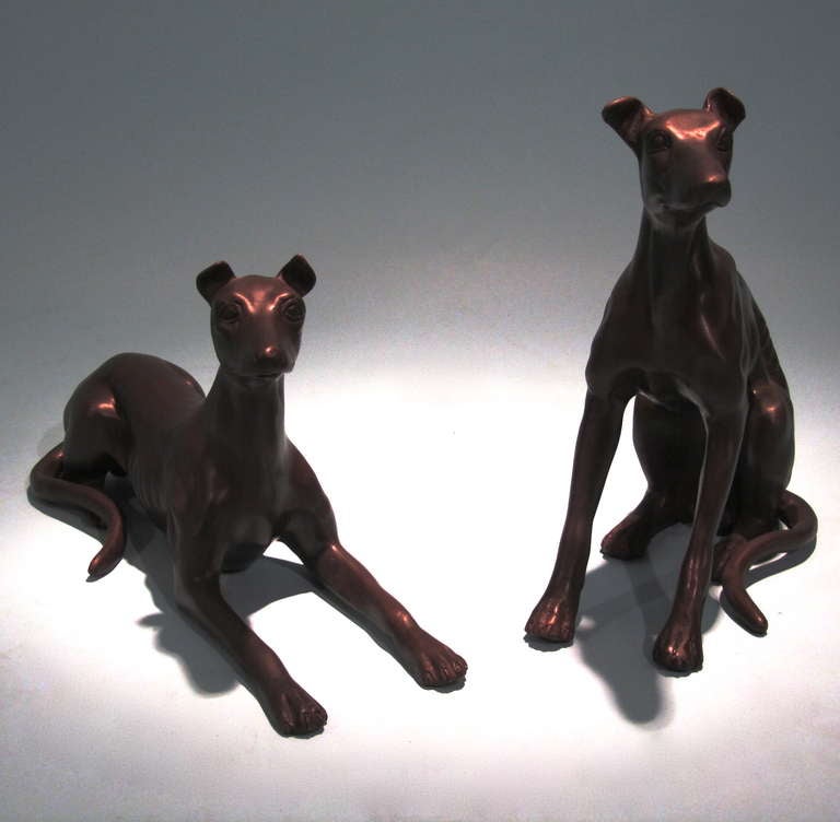 An elegant contemporary pair of bronze figures of greyhounds, one seated and one reclining. Both signed P. Riley.