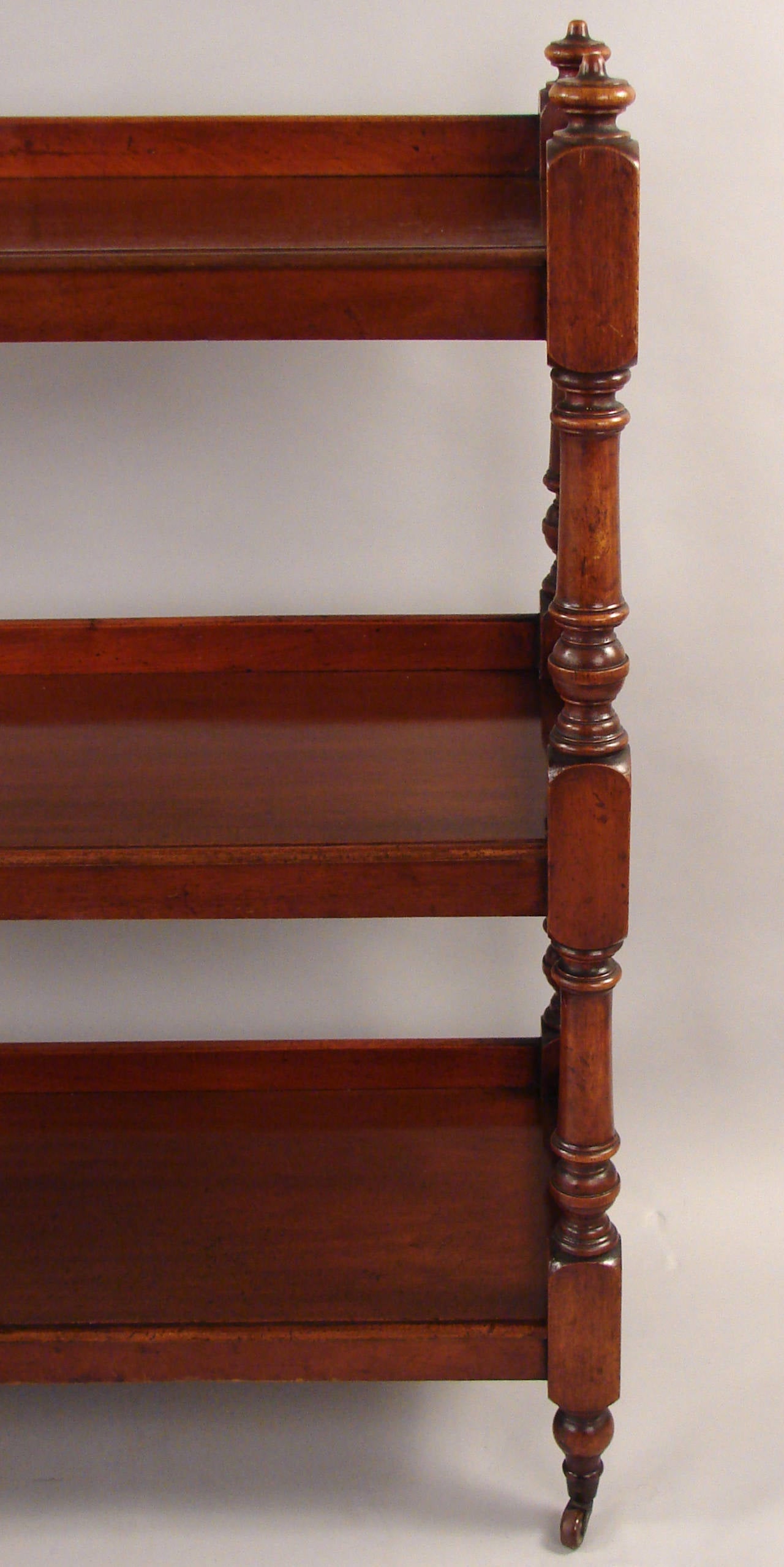 An English mahogany three-tier server or ètagerè, the top shelf with four finials at the corners, each shelf with a raised edge and turned standards ending in blocks, supported on similarly turned legs with porcelain casters.