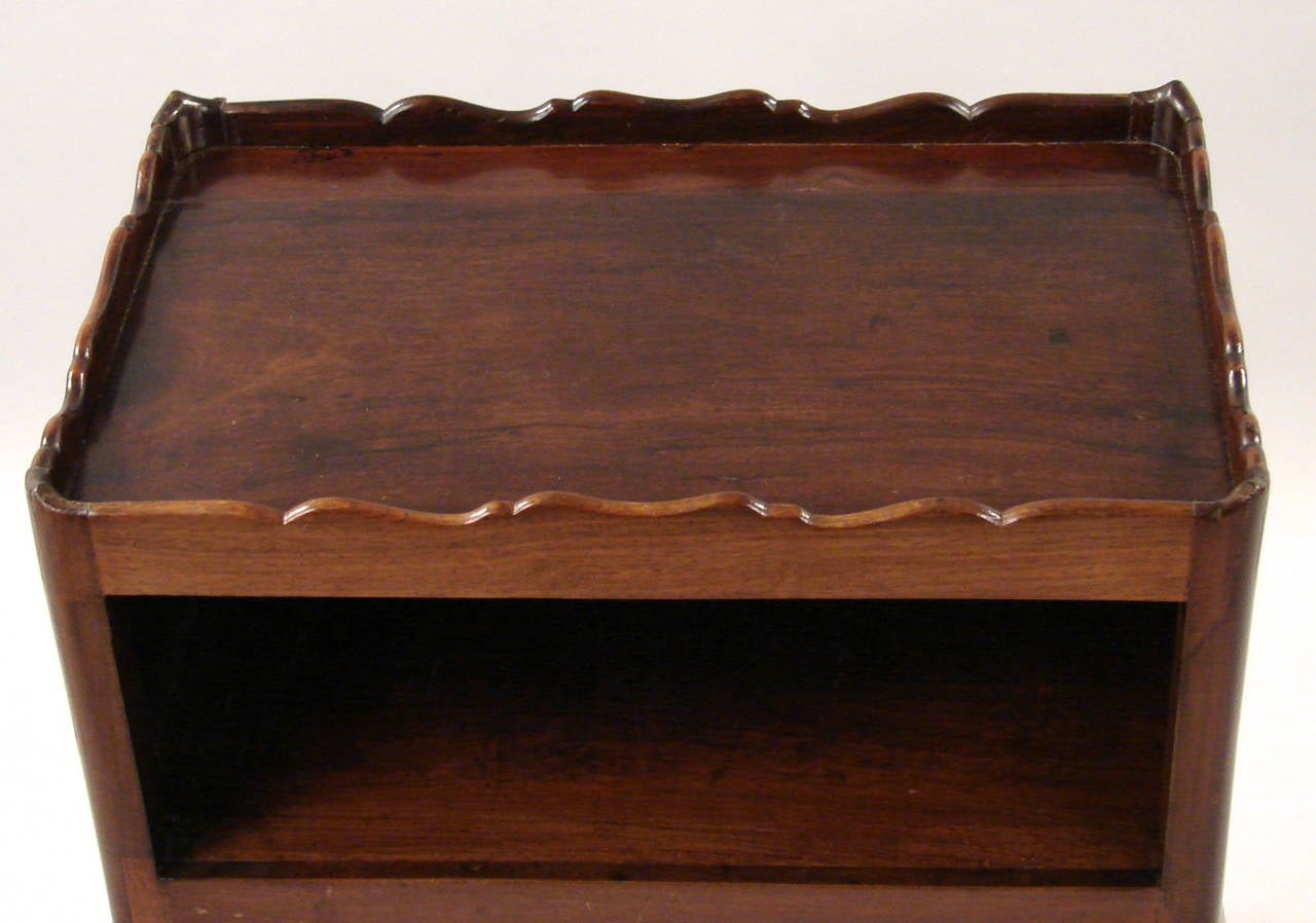A George II solid walnut bedside table having a rectangular top with a shaped gallery above an open shelf and rising on cabriole legs, circa 1750.
